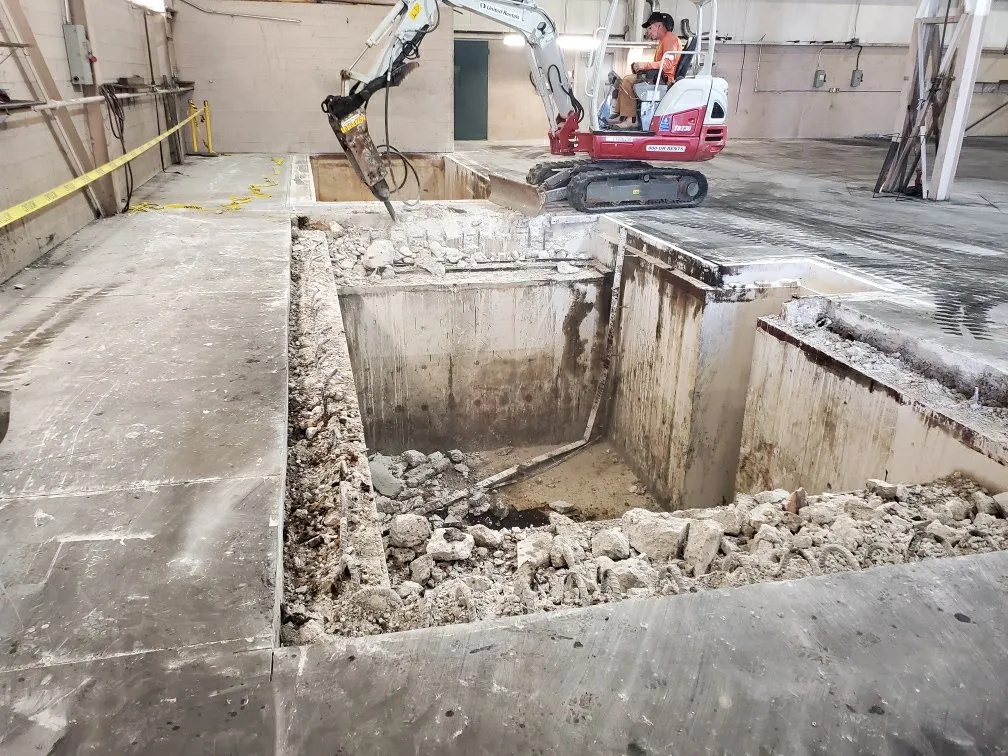 An excavator removing old concrete pits during a site remediation project inside a commercial building